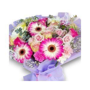 Bouquet de flores frescas con gerberas, rosas y claveles en tonos rosados y blancos, decorado con mariposas y envoltura en tonos pastel.