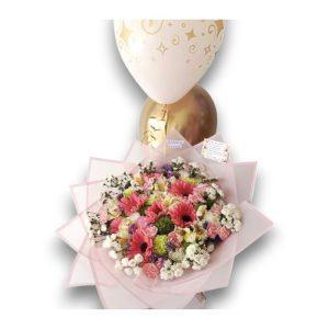 Elegante bouquet de flores frescas en tonos rosados y pastel acompañado de globos dorados, ideal para celebraciones especiales.
