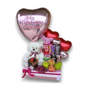 Caja en forma de corazón incluye un oso, frutas, mini pastel y globos decorativos.